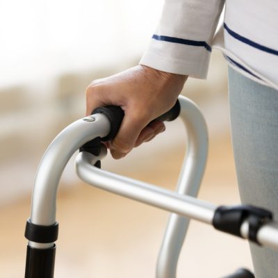 Close up disabled older woman holding hand on walker, rehabilitation and recovery after injury, mature patient moving, doing exercise with walking frame, standing indoor, walk training